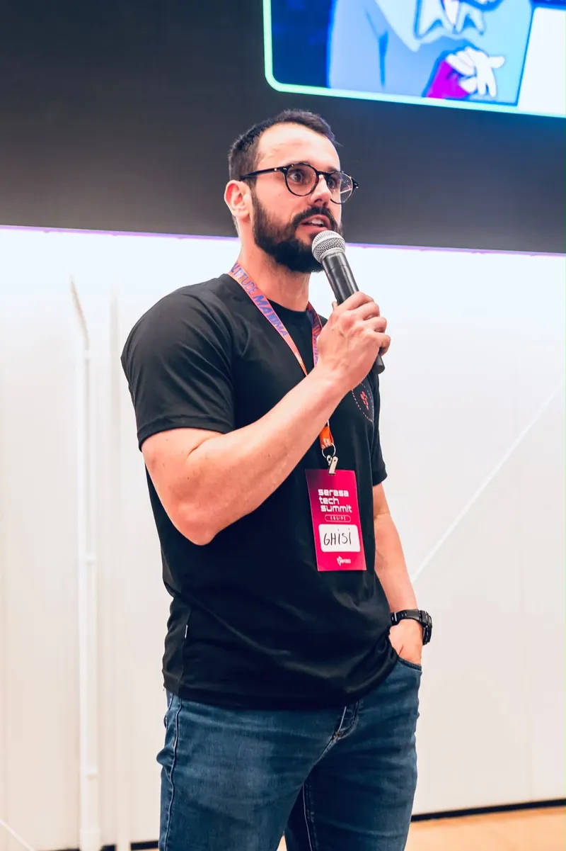 Fernando Ghisi falando ao microfone no palco do Serasa Tech Summit, com o crachá da equipe do evento