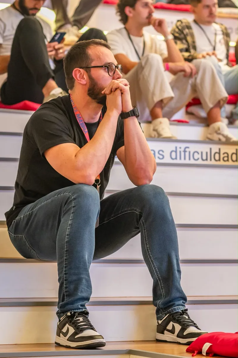 Fernando Ghisi sentado na arquibancada, atento a uma palestra, com outros participantes ao fundo